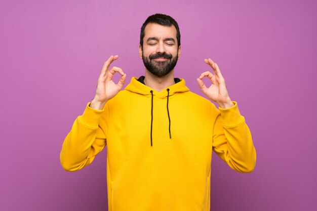 Hombre guapo con sudadera amarilla en pose zen