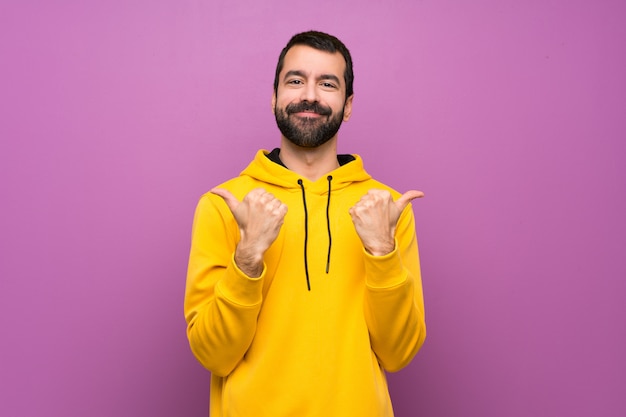 Hombre guapo con sudadera amarilla con pulgares arriba gesto y sonriendo