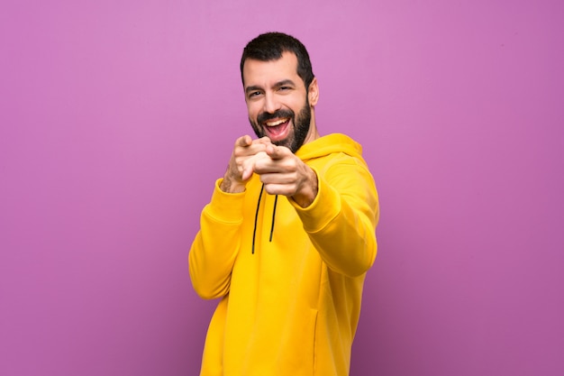 Hombre guapo con sudadera amarilla señala con el dedo mientras sonríe