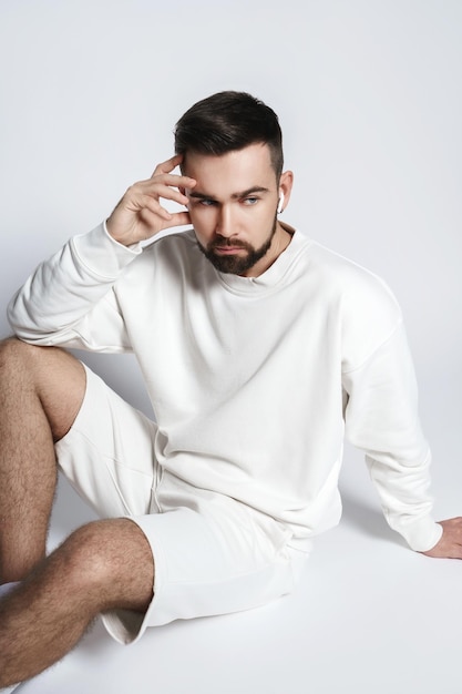 Hombre guapo con sudadera blanca y pantalones cortos con auriculares inalámbricos sentado