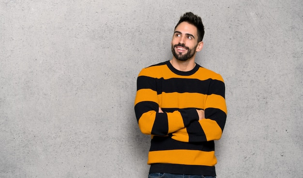 Hombre guapo con suéter a rayas mirando hacia arriba mientras sonríe sobre una pared con textura