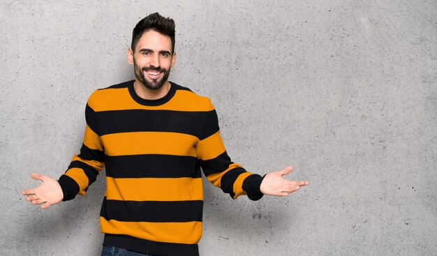 Hombre guapo con suéter a rayas sonriendo sobre pared con textura