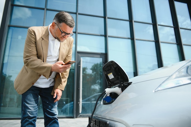 Hombre guapo con teléfono mientras se carga el coche