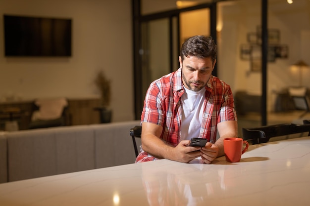 Hombre guapo con teléfono móvil sentado el fin de semana en casa hombre estadounidense usando el teléfono mientras está sentado en