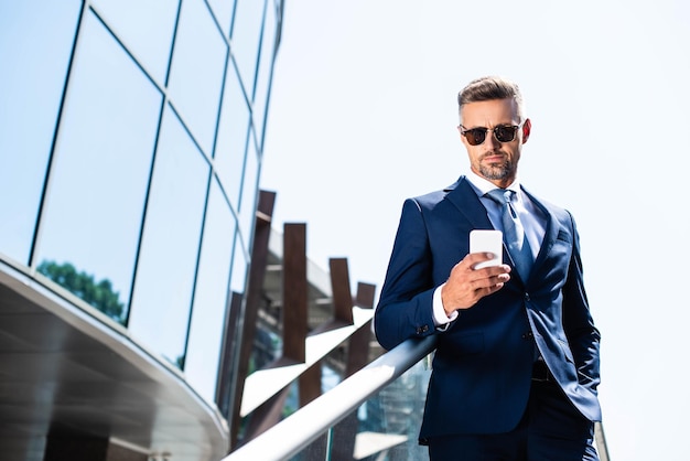 Foto hombre guapo en traje con la mano en el bolsillo con teléfono inteligente