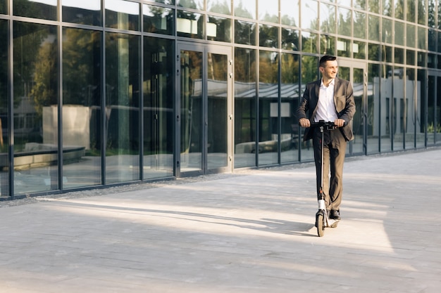 Hombre guapo en un traje montando scooter eléctrico en una ciudad empresario adulto montando con eléctrico