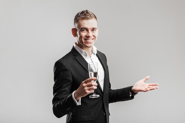 Foto hombre guapo en un traje de negocios sonríe y sostiene una copa de champán sobre un fondo blanco. tiempo de fiesta .