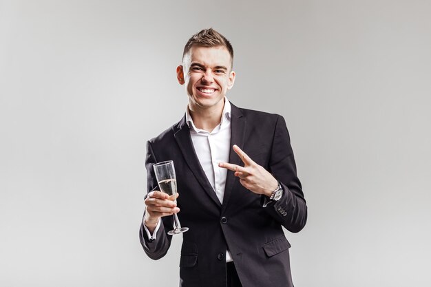 Foto hombre guapo en un traje de negocios sonríe y sostiene una copa de champán sobre un fondo blanco. tiempo de fiesta .