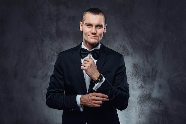 Un hombre guapo con traje negro abrochando botones en las mangas. Foto de estudio en una pared con textura oscura