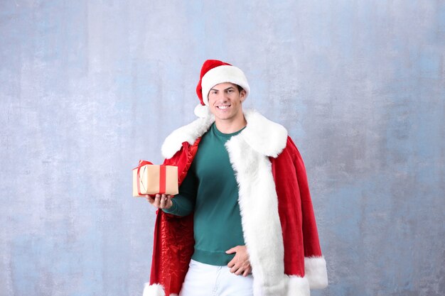 Hombre guapo en traje de Santa Claus con caja de regalo sobre fondo de color