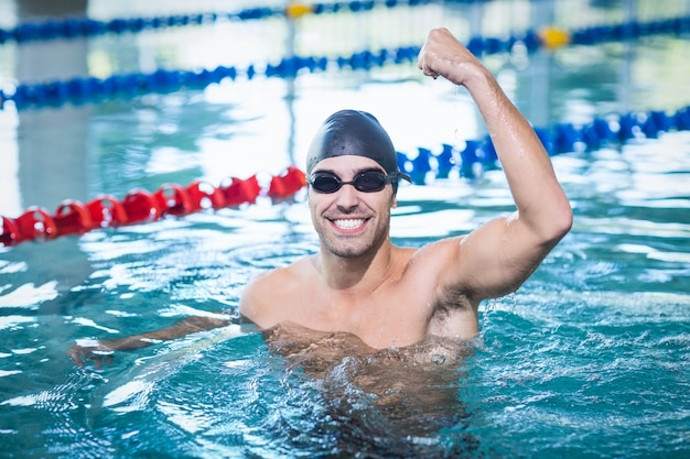 Hombre guapo triunfando con el brazo levantado en la piscina