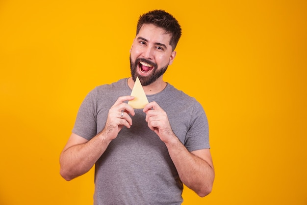 Hombre guapo con un trozo de queso sobre fondo amarillo. Chico con una rebanada de queso en la mano.