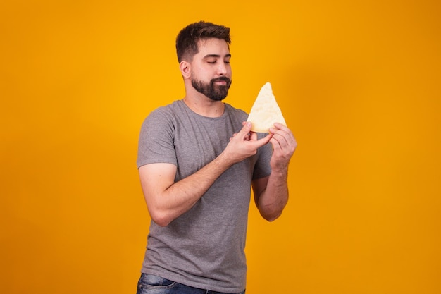 Hombre guapo con un trozo de queso sobre fondo amarillo. Chico con una rebanada de queso en la mano.