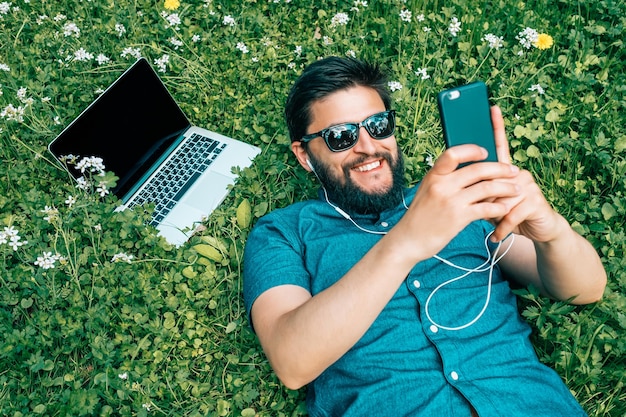 Hombre guapo tumbado en la hierba verde en el parque y escuchando música