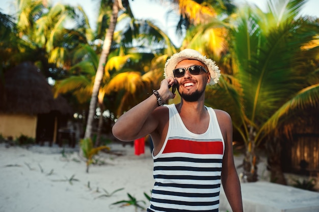 Hombre guapo turista hablando por teléfono inteligente contra el fondo de palmeras