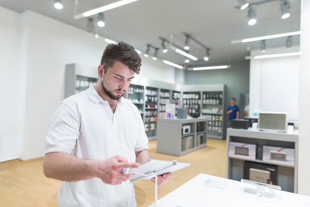 Hombre guapo usa una tableta en una tienda de electrónica