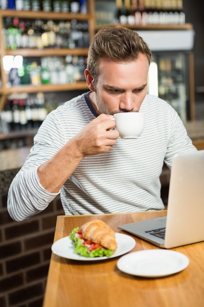 Hombre guapo usando laptop y tomando un café