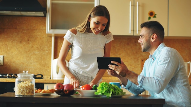 Hombre guapo usando tableta mientras su novia cocina