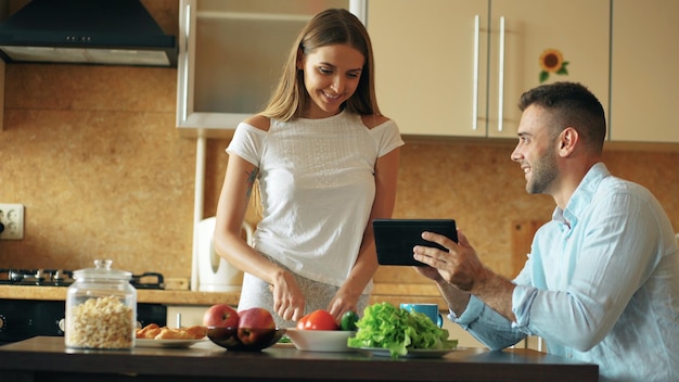 Hombre guapo usando tableta mientras su novia cocina