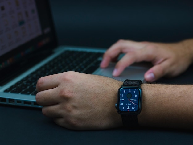 Hombre guapo y joven trabajando con reloj inteligente en la muneca en laptop