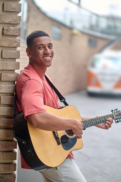 Hombre con guitarra cerca de la pared de ladrillo mirando a la cámara