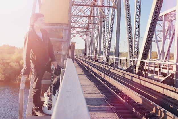 Un hombre con una guitarra eléctrica en el ferrocarril. Un músico con una chaqueta de cuero con una guitarra en la calle de la zona industrial. Guitarrista en el puente.