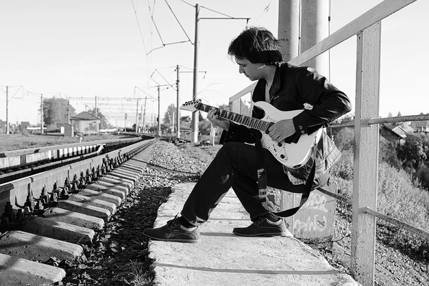 Un hombre con una guitarra eléctrica en el paisaje industrial monocromo al aire libre