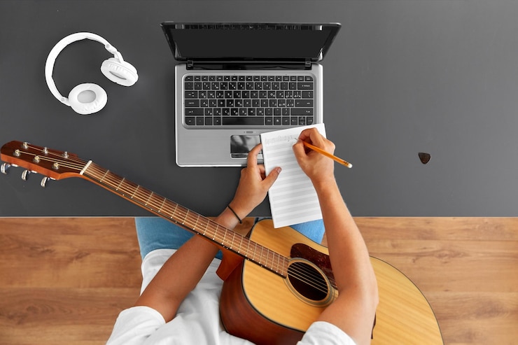 Foto hombre con guitarra escribiendo un libro de música en la mesa