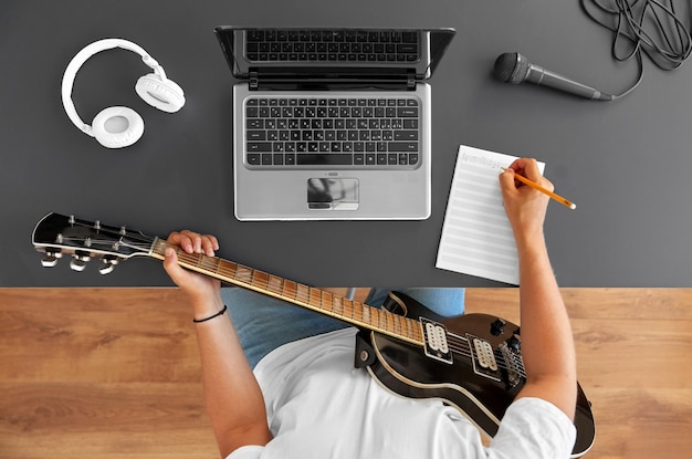 hombre con guitarra escribiendo un libro de música en la mesa