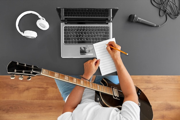 hombre con guitarra escribiendo un libro de música en la mesa