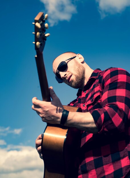 Hombre con guitarra en la naturaleza. Chico hipster relajante en un día de verano.