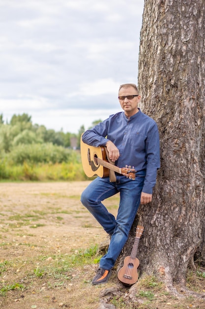 Foto un, hombre, con, un, guitarra, reclinado, contra, un, árbol