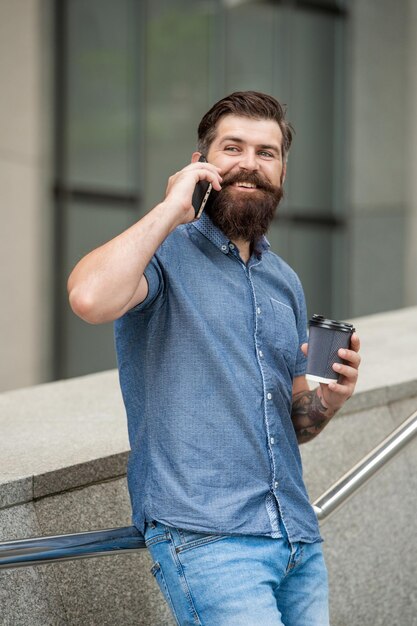 El hombre habla en el teléfono inteligente afuera, toma café, el hombre habla en el teléfono inteligente en la calle