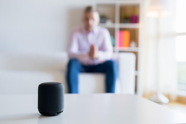 Hombre hablando con el altavoz inteligente del asistente virtual en la sala de estar