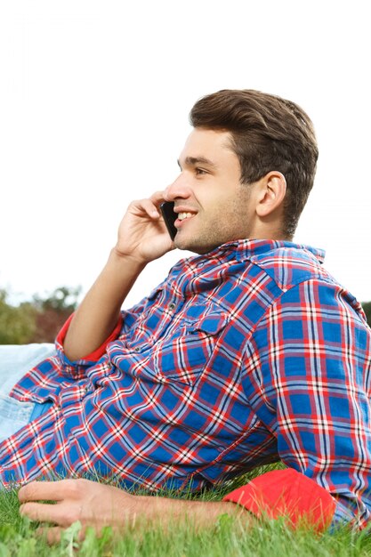 Hombre hablando por teléfono y sonriendo tirado en el pasto