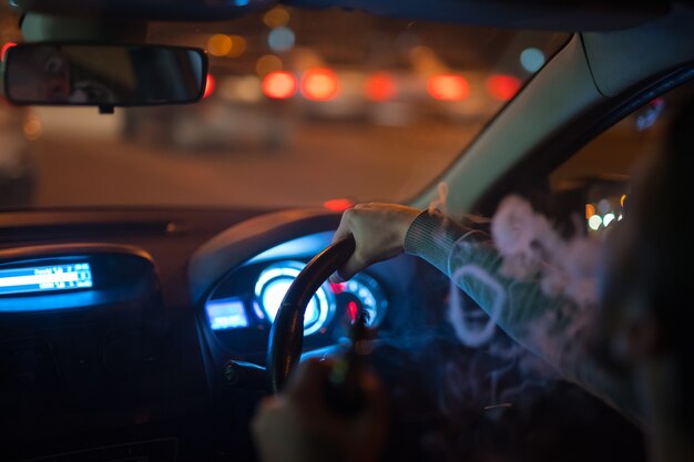 El hombre hace aros de humo en el coche. Por la noche, por la noche