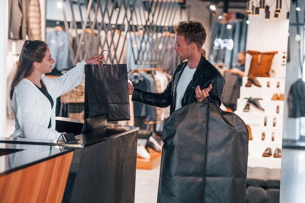 Foto el hombre hace la compra en una tienda moderna con ropa elegante la trabajadora sirve al chico en la caja