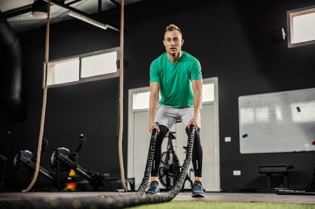 Un hombre hace ejercicio con cuerdas de batalla Un hombre entrena con cuerda de batalla en un gimnasio de crossfit interior aislado