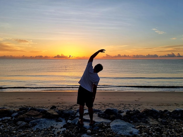El hombre hace ejercicio en la playa mientras sale el sol temprano en la mañana