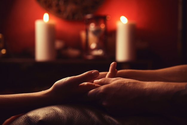 Un hombre hace que una mujer acupresión dedos. Masaje de manos con iluminación íntima.