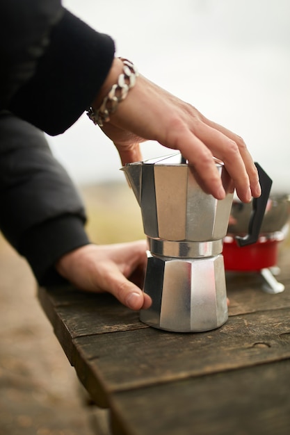 Hombre haciendo café para acampar al aire libre con cafetera géiser de metal sobre un quemador de gas, paso a paso.