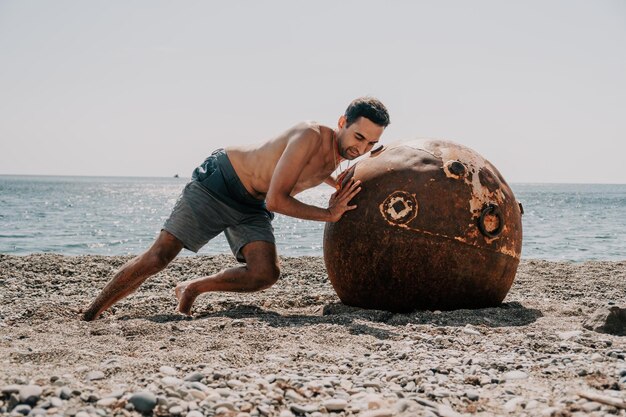 Hombre haciendo ejercicio al aire libre cerca de la vieja mina marina flotante oxidada en la playa con costa rocosa y