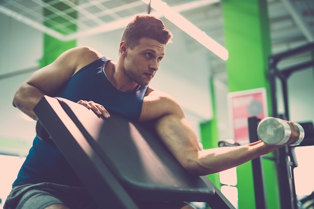 El hombre haciendo ejercicio de bíceps con una mancuerna en el gimnasio.