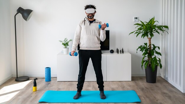 Hombre haciendo ejercicio con mancuernas con un auricular VR en casa trabajando en la fuerza de los brazos disfrutando de gafas de realidad virtual para practicar deporte Deportista levantando pesas sobre el interior de la sala de estar