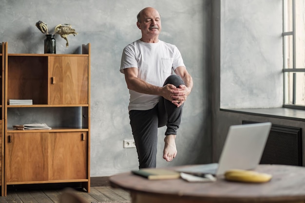 Hombre haciendo ejercicio de yoga en casa usando una lección en línea en un cuaderno