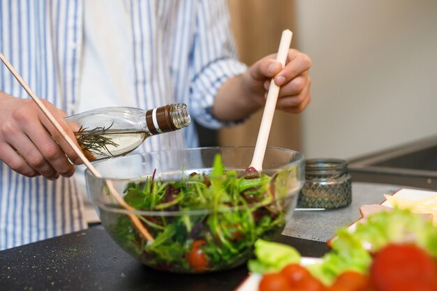 Hombre haciendo ensalada y usa aceite