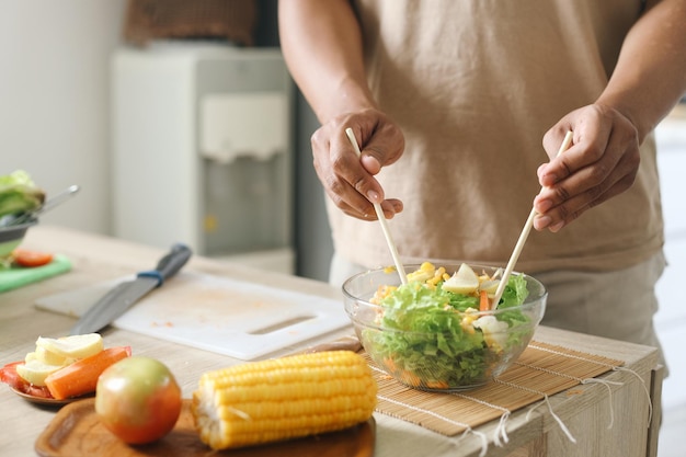 Hombre haciendo ensalada vegana fresca en la cocina en casa