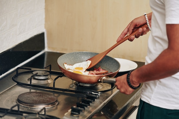 Hombre haciendo huevos fritos y tocino para el desayuno