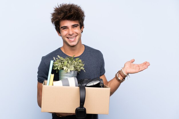 Hombre haciendo un movimiento mientras levanta una caja llena de cosas extendiendo las manos a un lado para invitar a venir