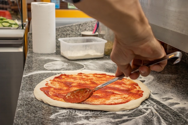 Un hombre haciendo una pizza margherita en un restaurante local de pizza y gyros.